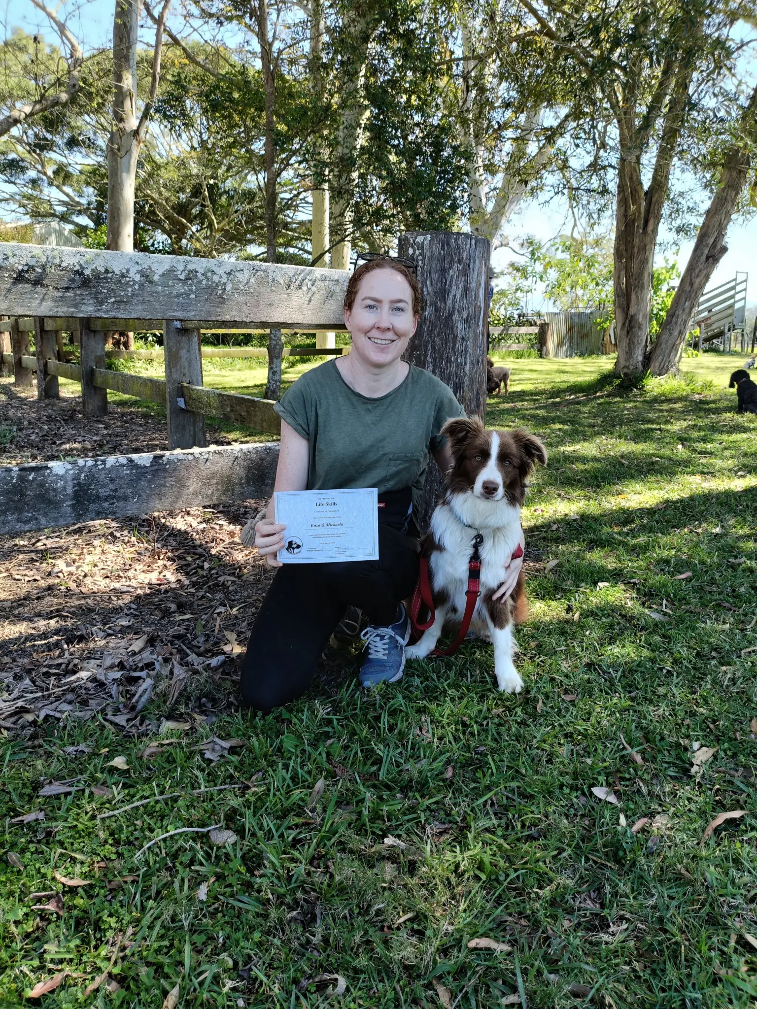 A handler kneels beside their dog while holding a Life Skills certificate.
